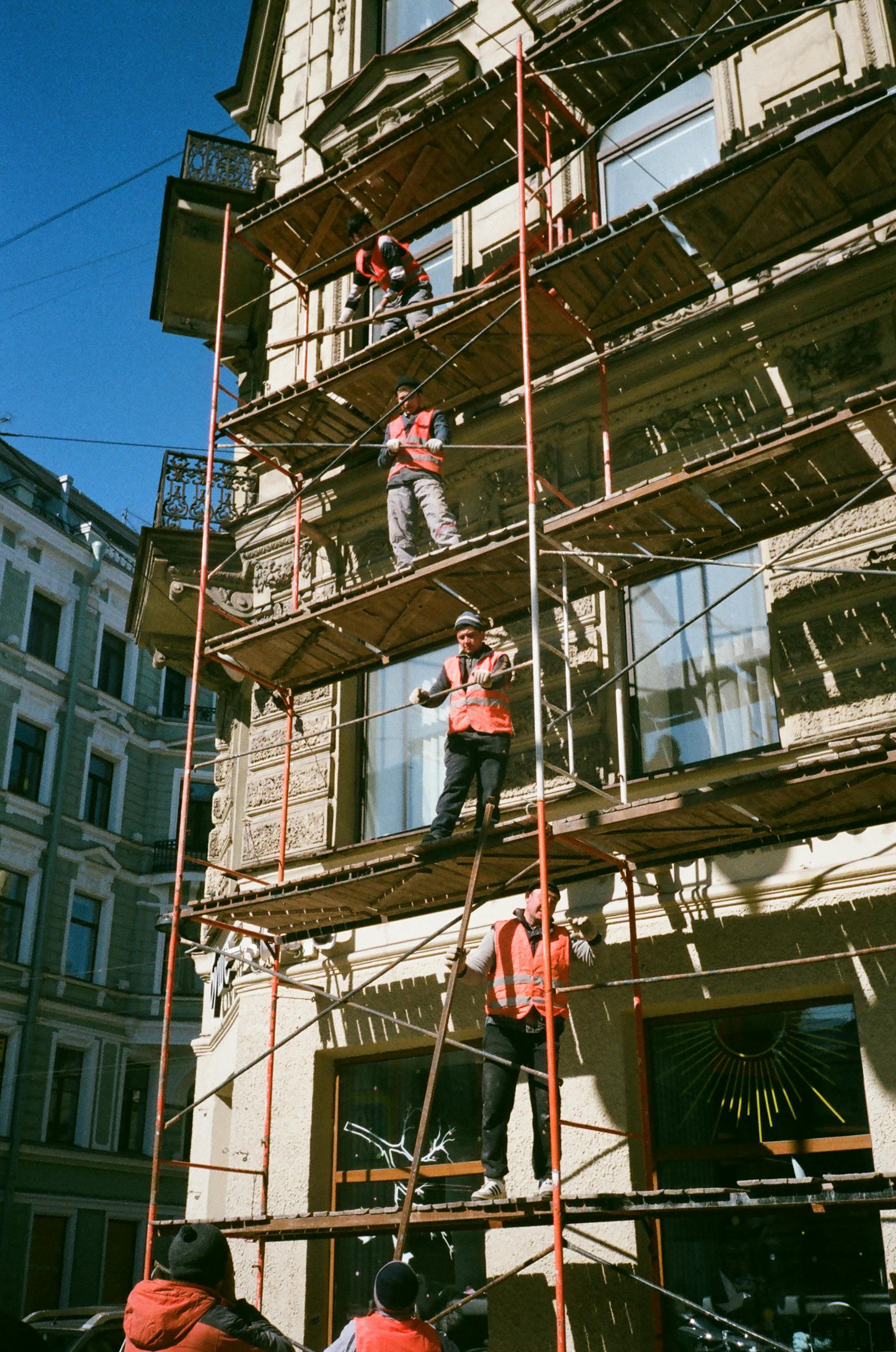 Construction workers on industrial scaffolding renovating a building facade on a sunny day.